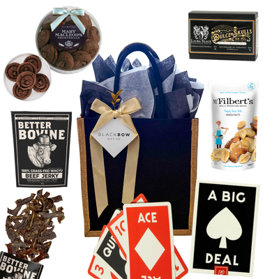 Shareable snack gift with oversized playing cards, chocolates, nuts, jerky, and hot chocolate, packaged in a black fabric tote.