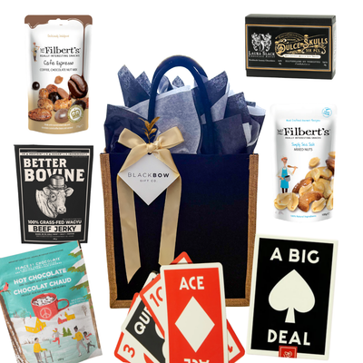 Shareable snack gift with oversized playing cards, chocolates, nuts, jerky, and hot chocolate, packaged in a black fabric tote.