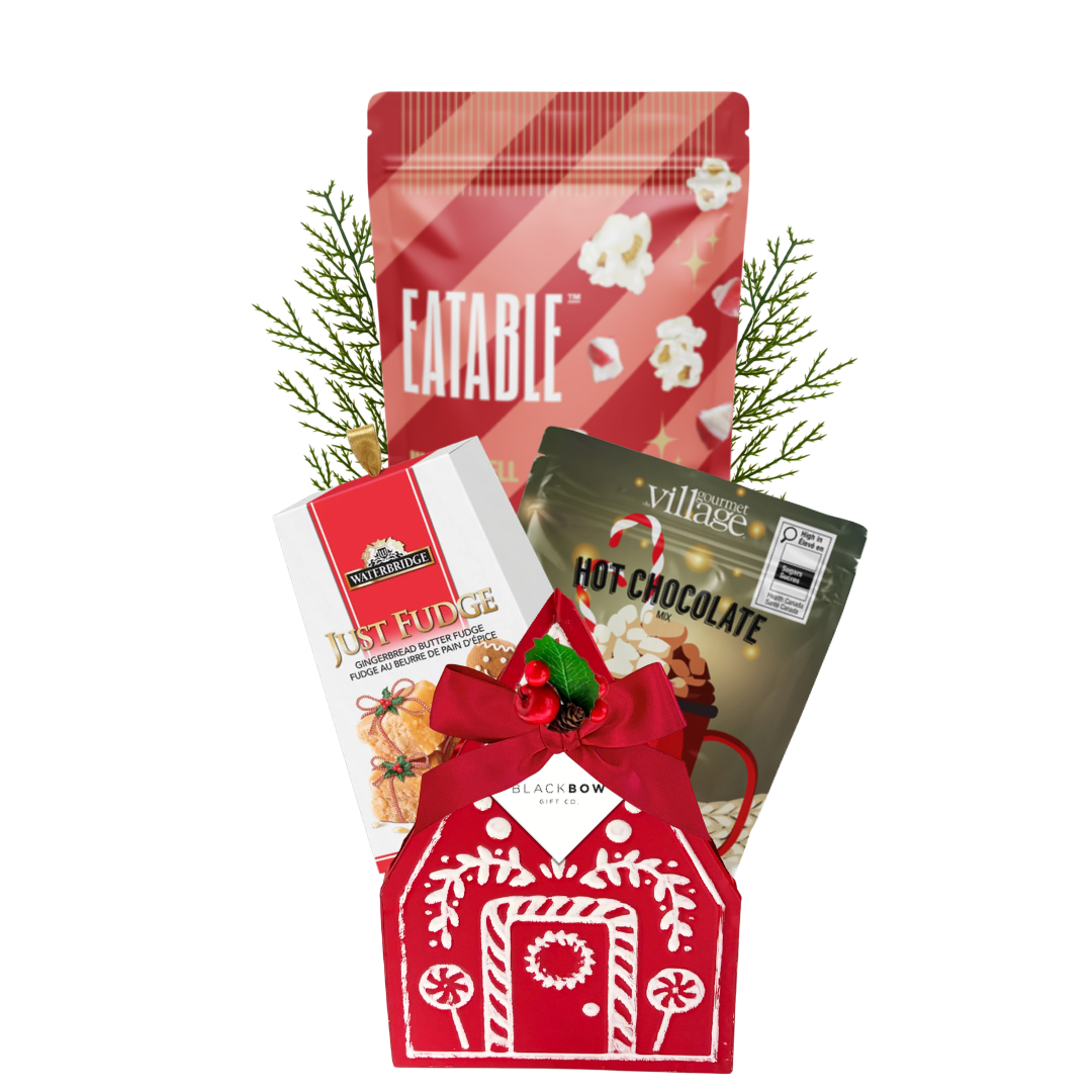 A Cozy Christmas holiday gift featuring a red gingerbread house keepsake filled with festive popcorn, hot chocolate mix, gingerbread fudge and seasonal greenery.