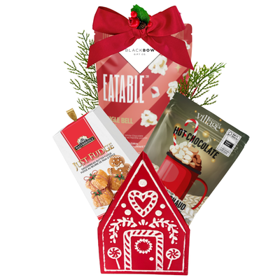 A Cozy Christmas holiday gift featuring a red gingerbread house keepsake filled with festive popcorn, hot chocolate mix, gingerbread fudge and seasonal greenery.