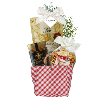 A Sweet Gesture gift featuring vanilla chai tea, gourmet honey and maple pecan crunch in a red gingham tote with ivory bow and Black Bow Gift Co. gift tag.