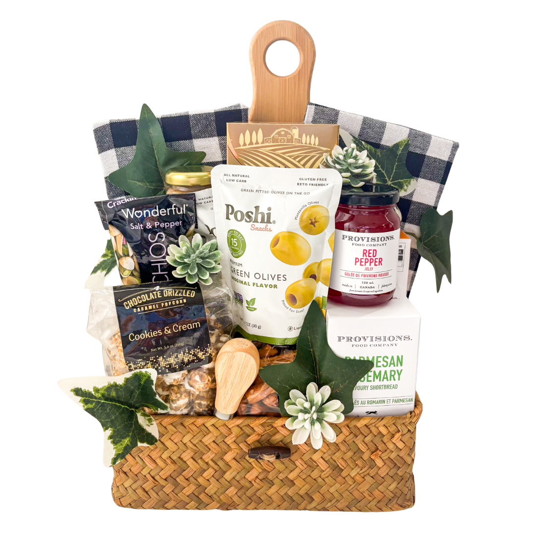 Woven picnic gift basket featuring a bamboo serving board, tea towels, gourmet snacks, olives, pistachios, popcorn, chocolates, and entertaining essentials by Black Bow Gift Co.

