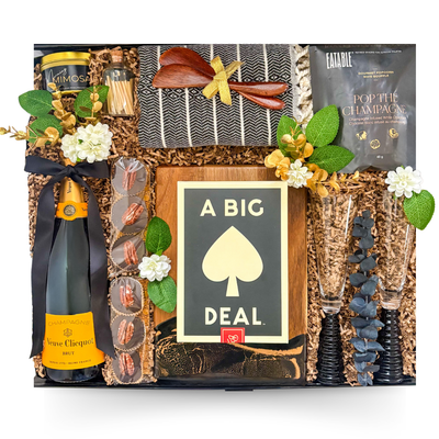 Luxury champagne celebration gift basket in a large high-gloss black magnetic keepsake gift box featuring Veuve Clicquot Champagne, champagne flutes, gourmet foods, artisan entertaining essentials, charcuterie board, and premium keepsakes.