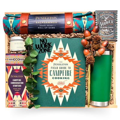 Luxury campfire-themed gift box with Pendleton campfire cooking book, backgammon set, gourmet treats, travel tumbler, candle, and games in wooden keepsake box.