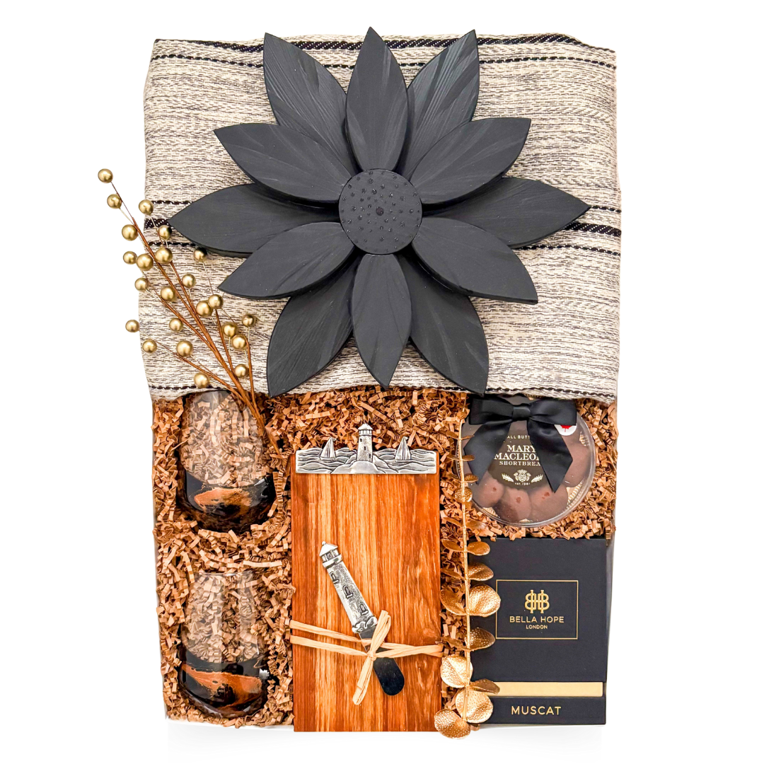 Luxury couple gift with blanket, candle, wine glasses, Nova Scotia-themed board, cheese knife, and chocolate treats, styled for cozy, sensory coastal indulgence.