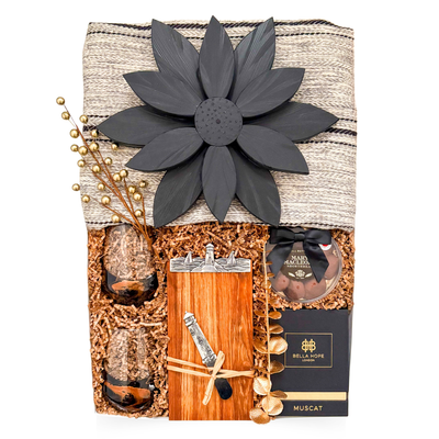 Luxury couple gift with blanket, candle, wine glasses, Nova Scotia-themed board, cheese knife, and chocolate treats, styled for cozy, sensory coastal indulgence.