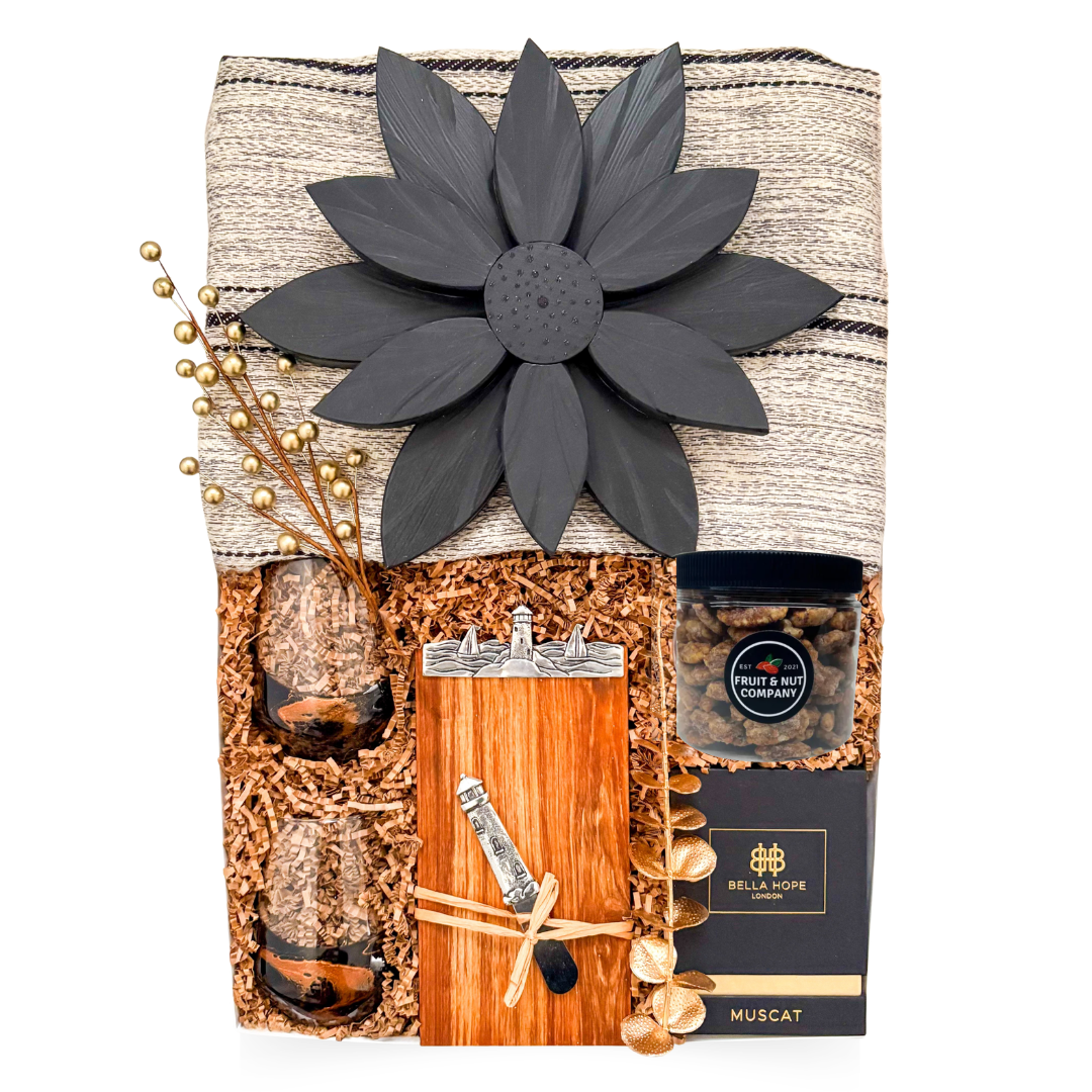 Luxury couple gift with blanket, candle, wine glasses, Nova Scotia-themed board, cheese knife, and chocolate treats, styled for cozy, sensory coastal indulgence.