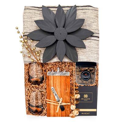 Luxury couple gift with blanket, candle, wine glasses, Nova Scotia-themed board, cheese knife, and chocolate treats, styled for cozy, sensory coastal indulgence.