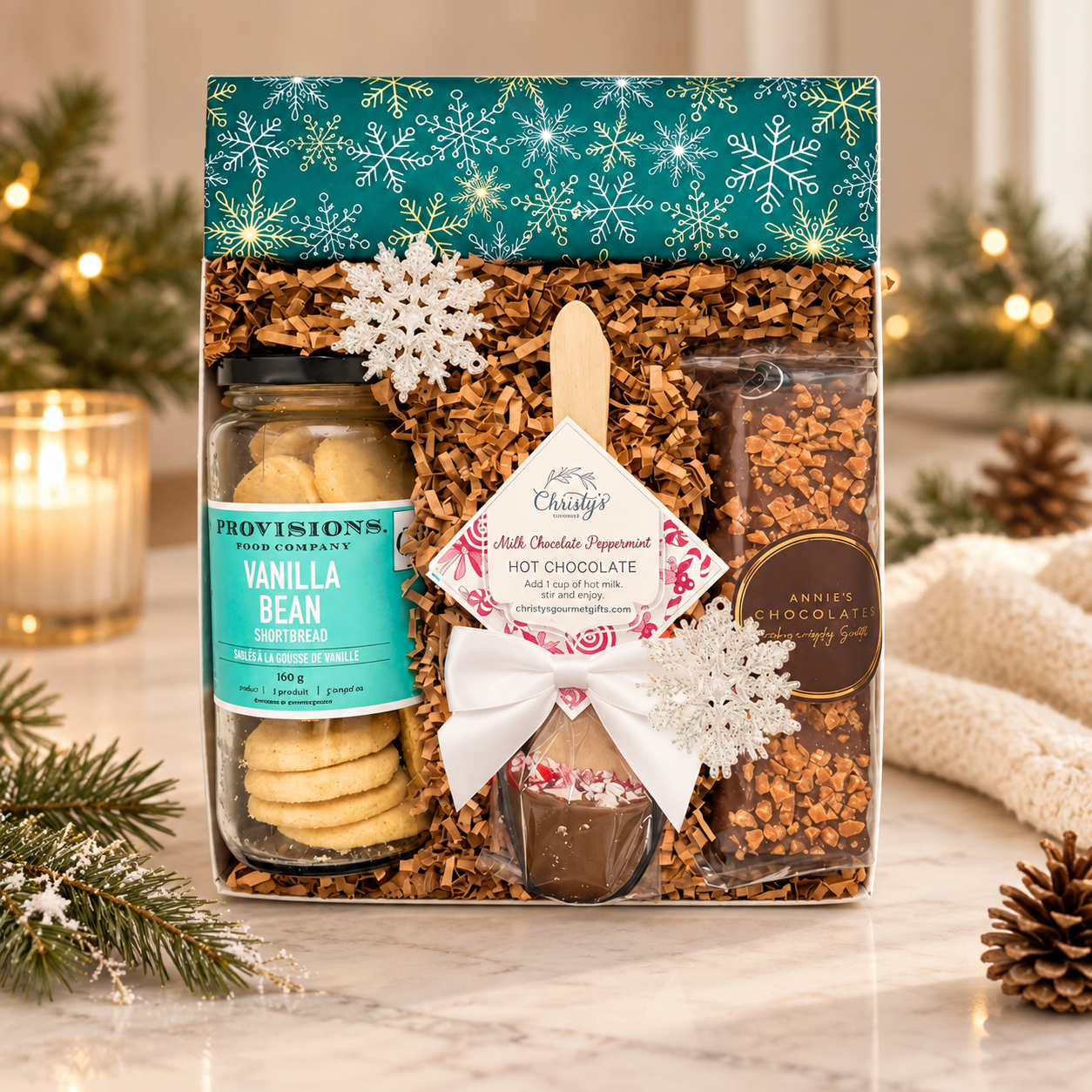 Elegant winter gift box featuring vanilla bean shortbread, peppermint hot chocolate and artisan chocolates, styled with warm lighting, evergreen accents and sophisticated seasonal décor.