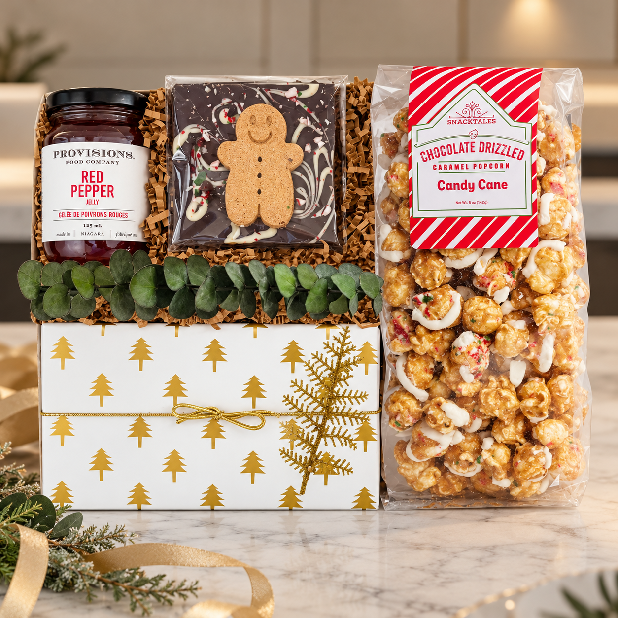 Elegant holiday gift box with gold tree detailing, featuring red pepper jelly, gingerbread chocolate bark, and candy cane caramel popcorn, styled in a sophisticated, minimalist setting.