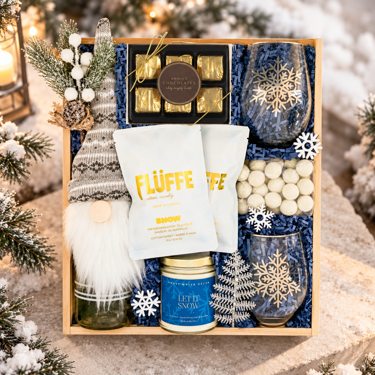 Luxury winter gift box featuring a cozy gnome, snowflake glasses, artisan chocolates, marshmallow treats, cotton candy, and a Let It Snow candle, styled with snowy evergreens and warm lantern light.