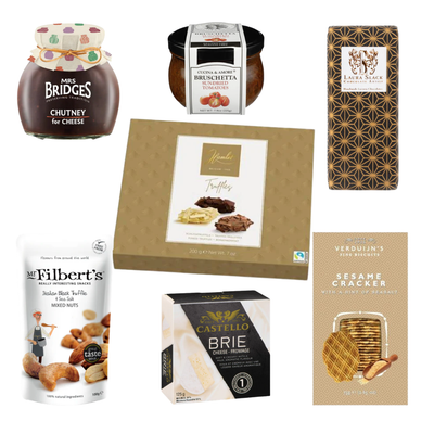 A flat-lay arrangement of gourmet food products against a white background. The items include Mrs. Bridges Chutney for Cheese, Cucina & Amore Sun-Dried Tomato Bruschetta, Laura Slack artisan chocolate, a box of Hamlet Truffles, Mr. Filbert's Italian Black Truffle & Sea Salt Mixed Nuts, a box of Castello Brie Cheese, and Verduijn's Sesame Crackers.