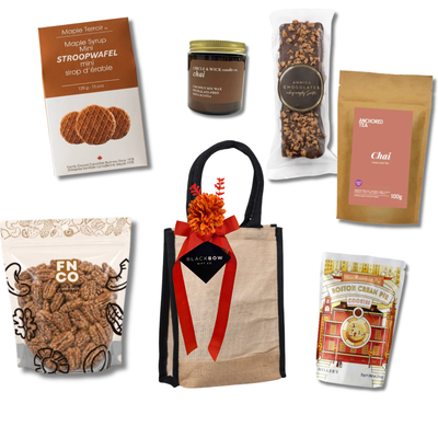 Enjoy gourmet gift basket with tea, cookies, maple stroopwafels, maple cinnamon pecans, chocolate and a cozy candle presented in a reusable tote by Black Bow Gift Co.