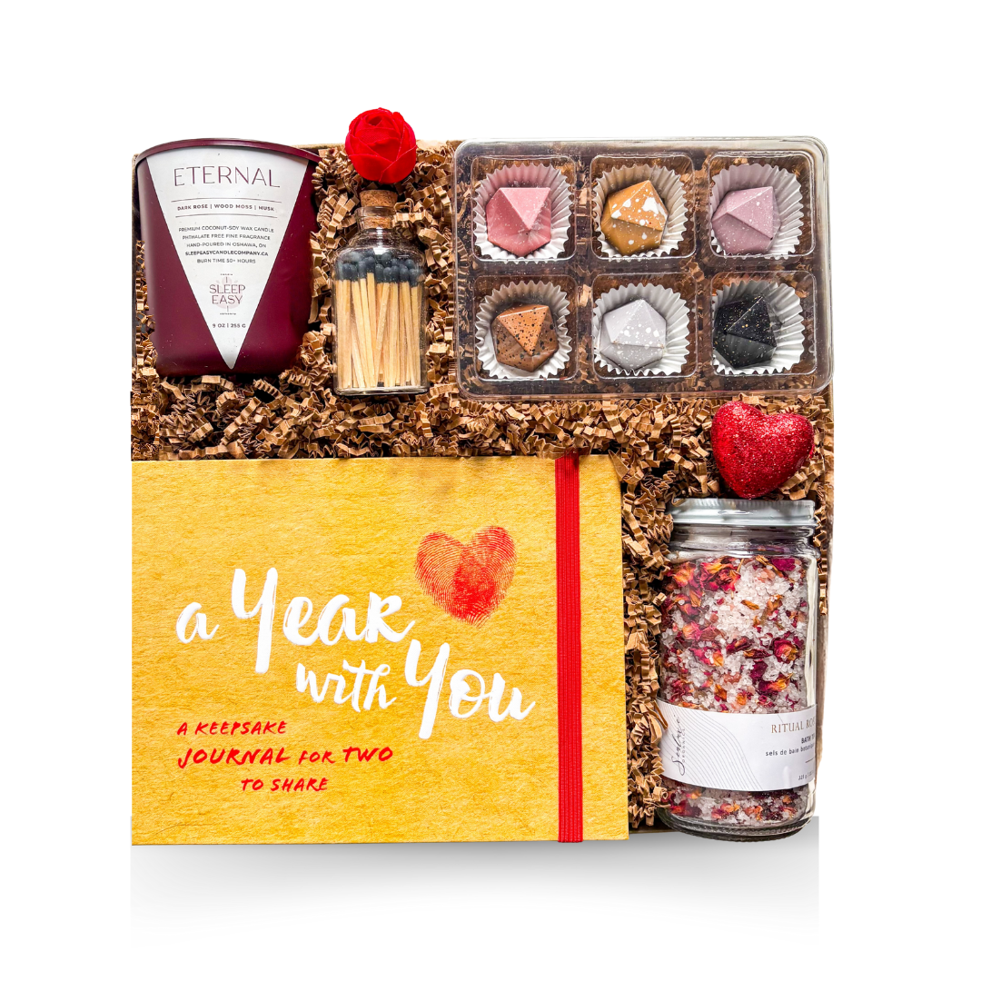 A premium keepsake gift box wrapped with luxury packaging details, revealing a romantic assortment including a candle with matches, hand-painted caramels, a couples keepsake journal, and a rose bath tea jar—styled for an elegant, sentimental unboxing experience.