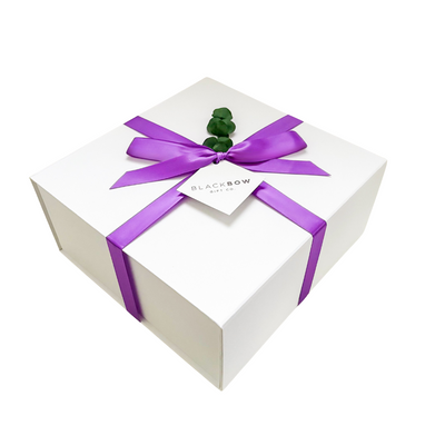 White gift box with a purple ribbon and greenery on a white background