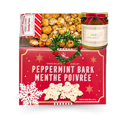 Festive Christmas gift basket featuring peppermint bark, caramel popcorn, winter-themed dark chocolate hot cocoa packets, and a holiday-scented candle.