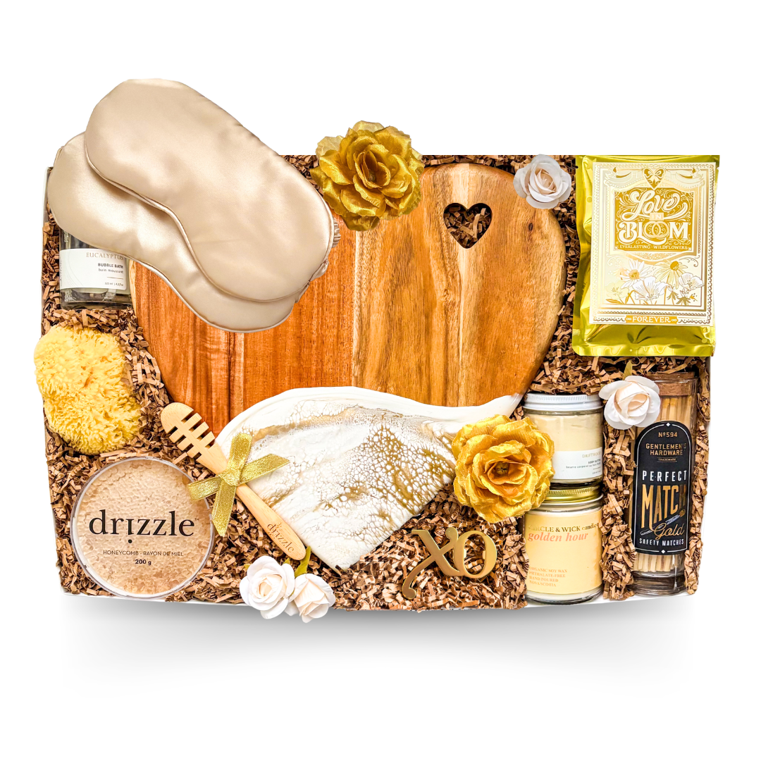 XL luxury keepsake gift box featuring a heart-shaped serving board, resin heart dish, silk sleep masks, bubble bath, candle, honey, sponge, bottle opener, safety matches, gourmet treats, olives, crackers, and charcuterie favourites.

