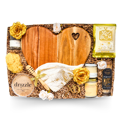 XL luxury keepsake gift box featuring a heart-shaped serving board, resin heart dish, silk sleep masks, bubble bath, candle, honey, sponge, bottle opener, safety matches, gourmet treats, olives, crackers, and charcuterie favourites.
