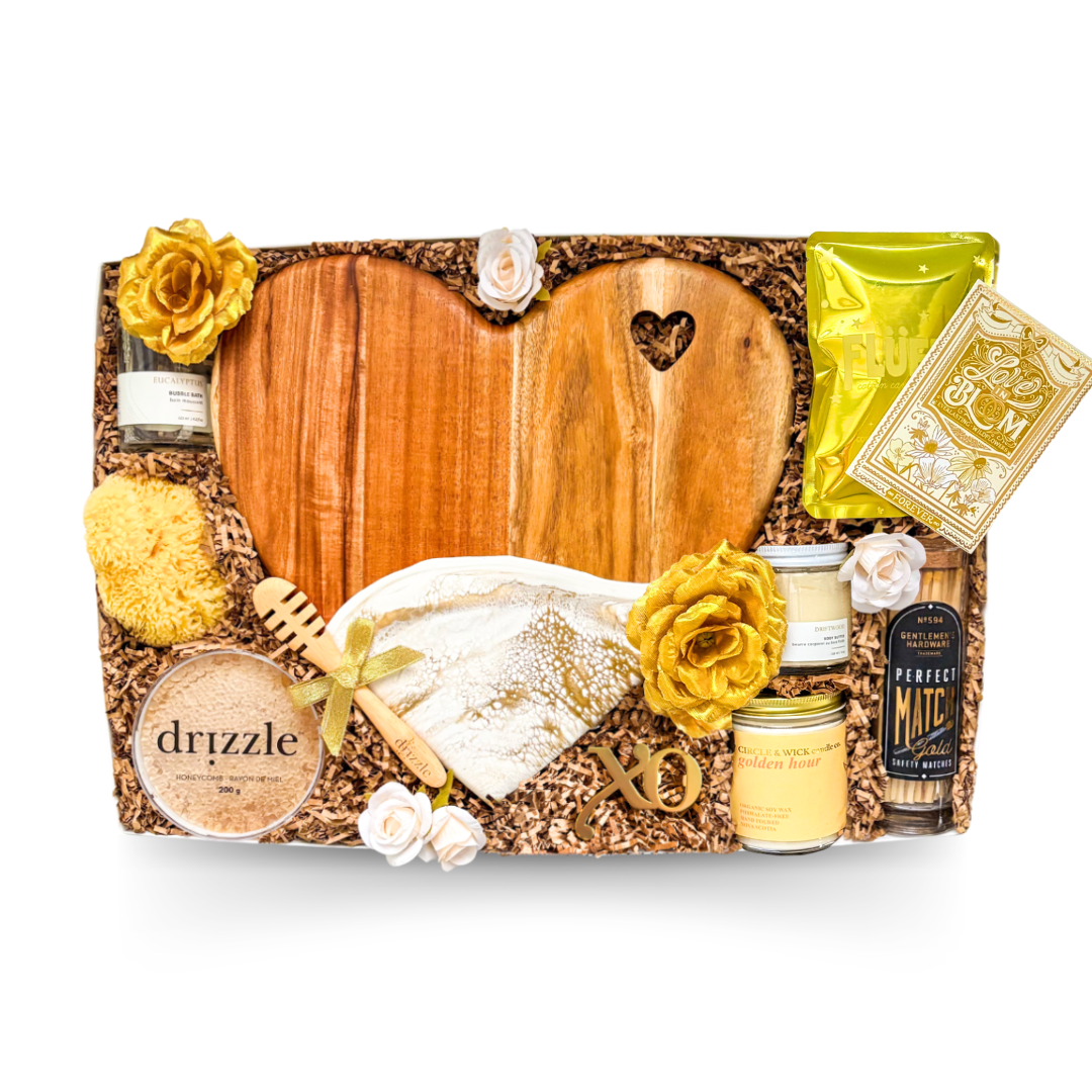 XL luxury keepsake gift box featuring a heart-shaped serving board, resin heart dish, silk sleep masks, bubble bath, candle, honey, sponge, bottle opener, safety matches, gourmet treats, olives, crackers, and charcuterie favourites.
