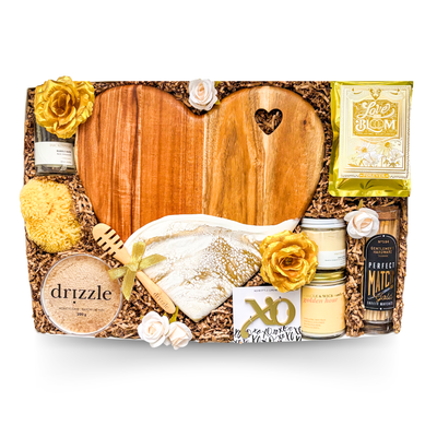 XL luxury keepsake gift box featuring a heart-shaped serving board, resin heart dish, silk sleep masks, bubble bath, candle, honey, sponge, bottle opener, safety matches, gourmet treats, olives, crackers, and charcuterie favourites.
