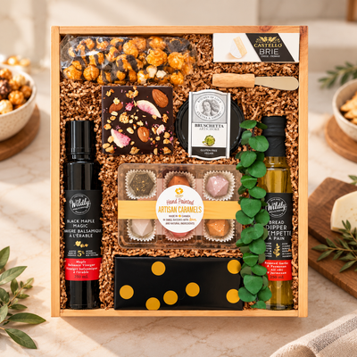 Luxury gourmet gift box featuring artisan caramels, chocolate popcorn, dark chocolate bark, Brie cheese, artichoke bruschetta, maple balsamic vinegar and bread dipper, styled in a modern kitchen