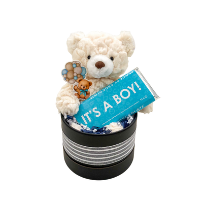 Keepsake baby boy gift with fluffy teddy bear and “It’s a Boy” chocolate, packaged in a round basket box.