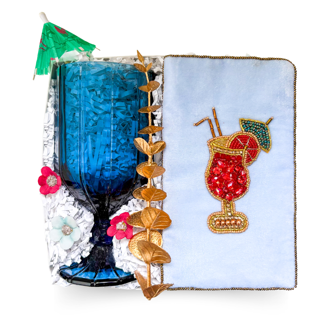 Luxury gift box featuring a blue stemmed goblet, embellished cocktail-themed eyeglass case, decorative gold accents, and a choice of premium alcoholic or non-alcoholic beverage.

