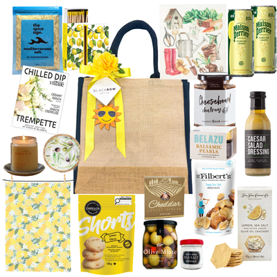 Lemon & Leisure summer gift tote with lemon-themed treats, Mediterranean snacks, crackers, olives, dips, sparkling beverages, and optional puzzle add-on for family gifting.