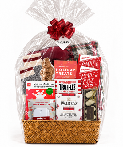 The Brr Basket holiday gift basket by Black Bow Gift Co., filled with cozy winter essentials and festive treats, wrapped in clear cellophane with a red bow, displayed in a luxurious Christmas living room.