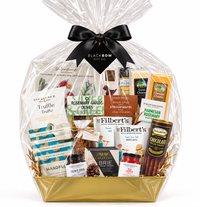 Luxury gourmet gift basket featuring artisan cheeses, crackers, olives, nuts, chocolates and savoury treats in a gold basket, wrapped in clear cellophane with a black satin bow and Black Bow Gift Co. tag, displayed on an elegant marble countertop in a sophisticated home setting.