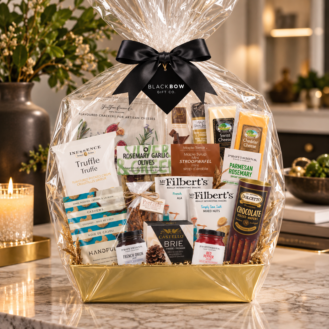 Luxury gourmet gift basket featuring artisan cheeses, crackers, olives, nuts, chocolates and savoury treats in a gold basket, wrapped in clear cellophane with a black satin bow and Black Bow Gift Co. tag, displayed on an elegant marble countertop in a sophisticated home setting.