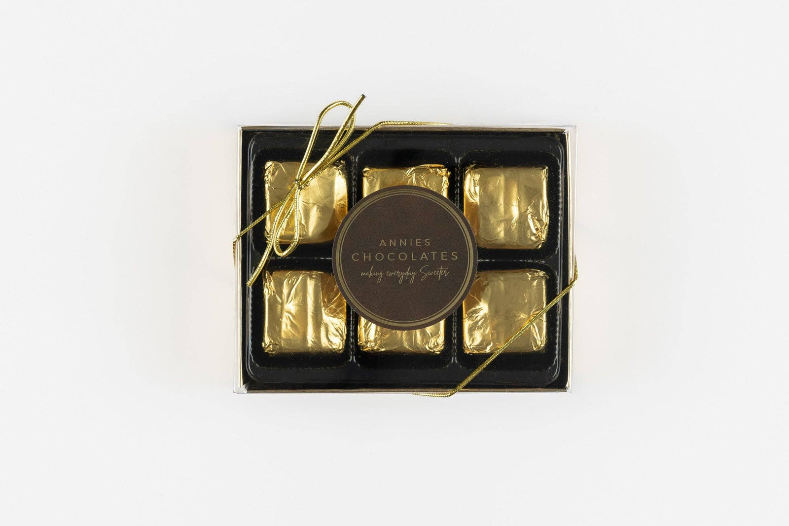 6 piece Annie’s Chocolates smooth milk chocolate wrapped in gold foil and placed in a box with clear lid.