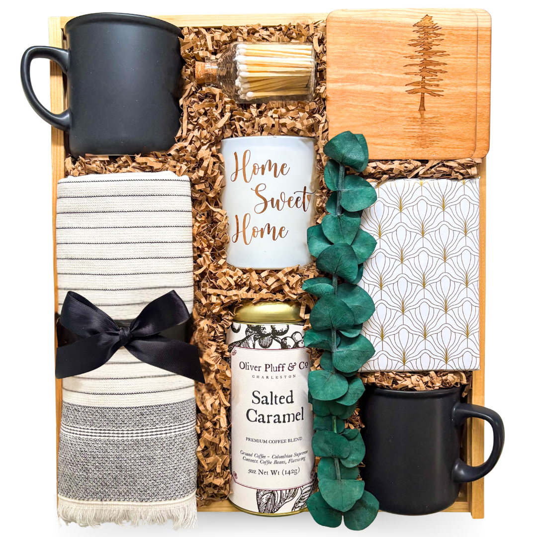 Premium wooden box gift featuring two black ceramic mugs, Home Sweet Home candle, gourmet coffee, striped tea towel, engraved wood coaster, decorative notebook, eucalyptus accent, and home-inspired keepsakes.
