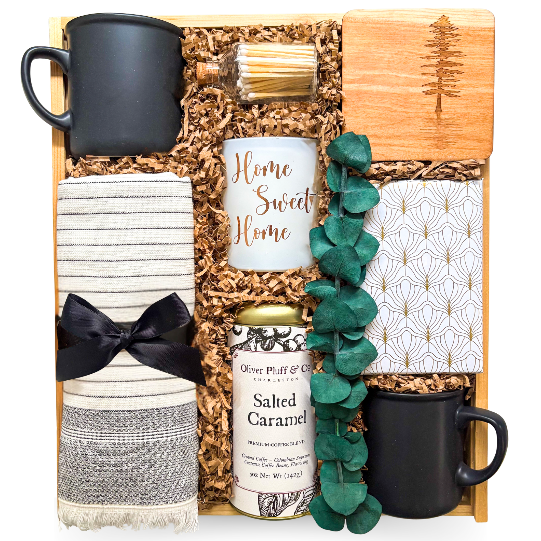 Premium wooden box gift featuring two black ceramic mugs, Home Sweet Home candle, gourmet coffee, striped tea towel, engraved wood coaster, decorative notebook, eucalyptus accent, and home-inspired keepsakes.


