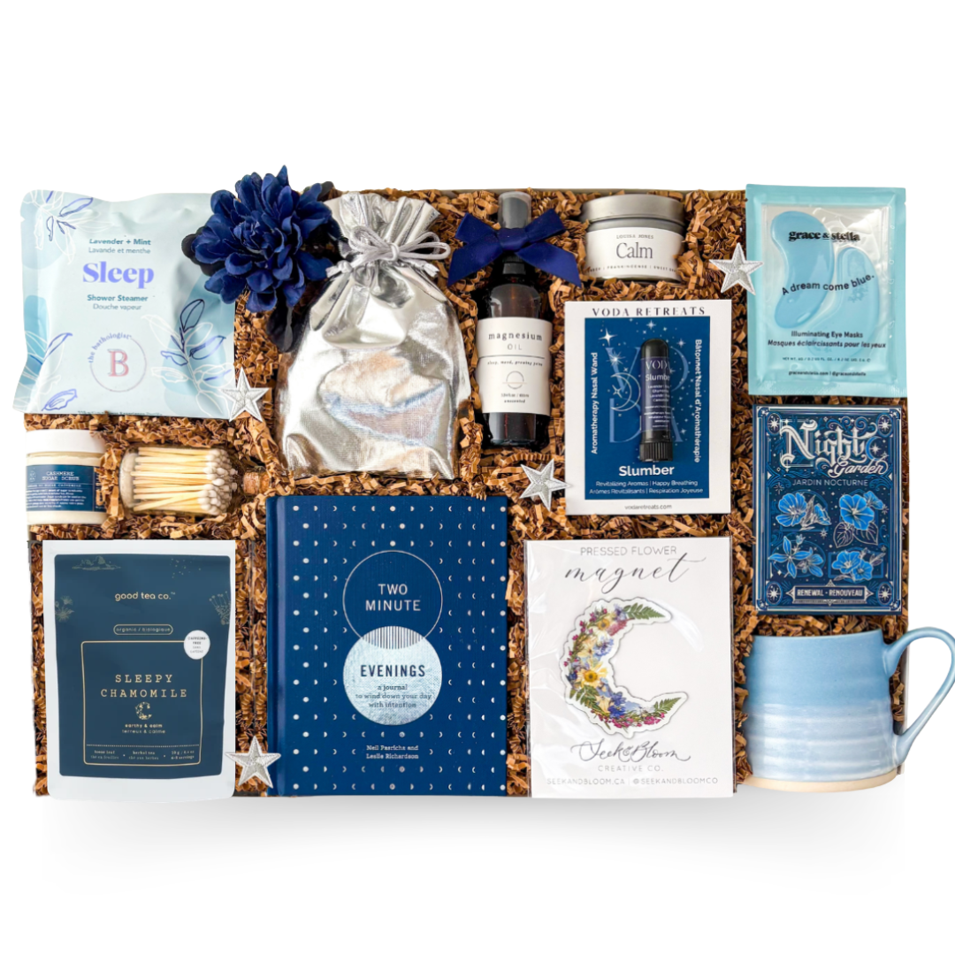 Gifting box with wellness products including tea, candles, and books on a white background