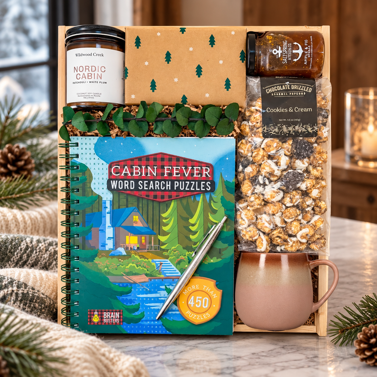 Winter gift box featuring a Nordic Cabin candle, cozy mug, Cabin Fever puzzle book, gourmet popcorn, apple and fig spread, and seasonal treats in an elegant winter setting.