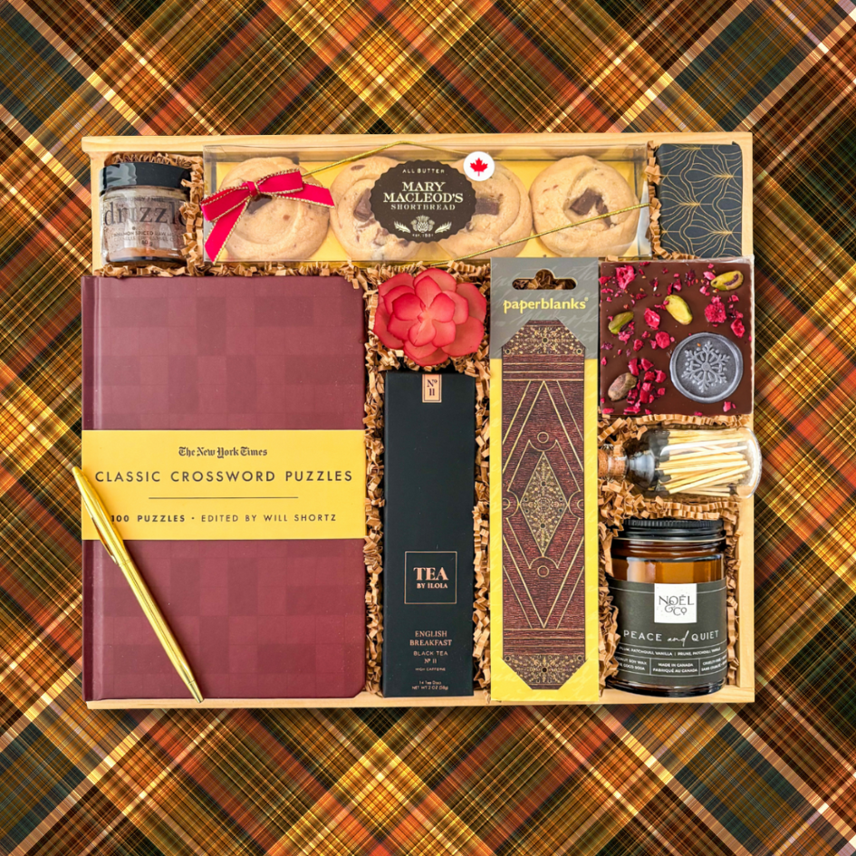Gift box with various items including a notebook, tea, and candles on a plaid background
