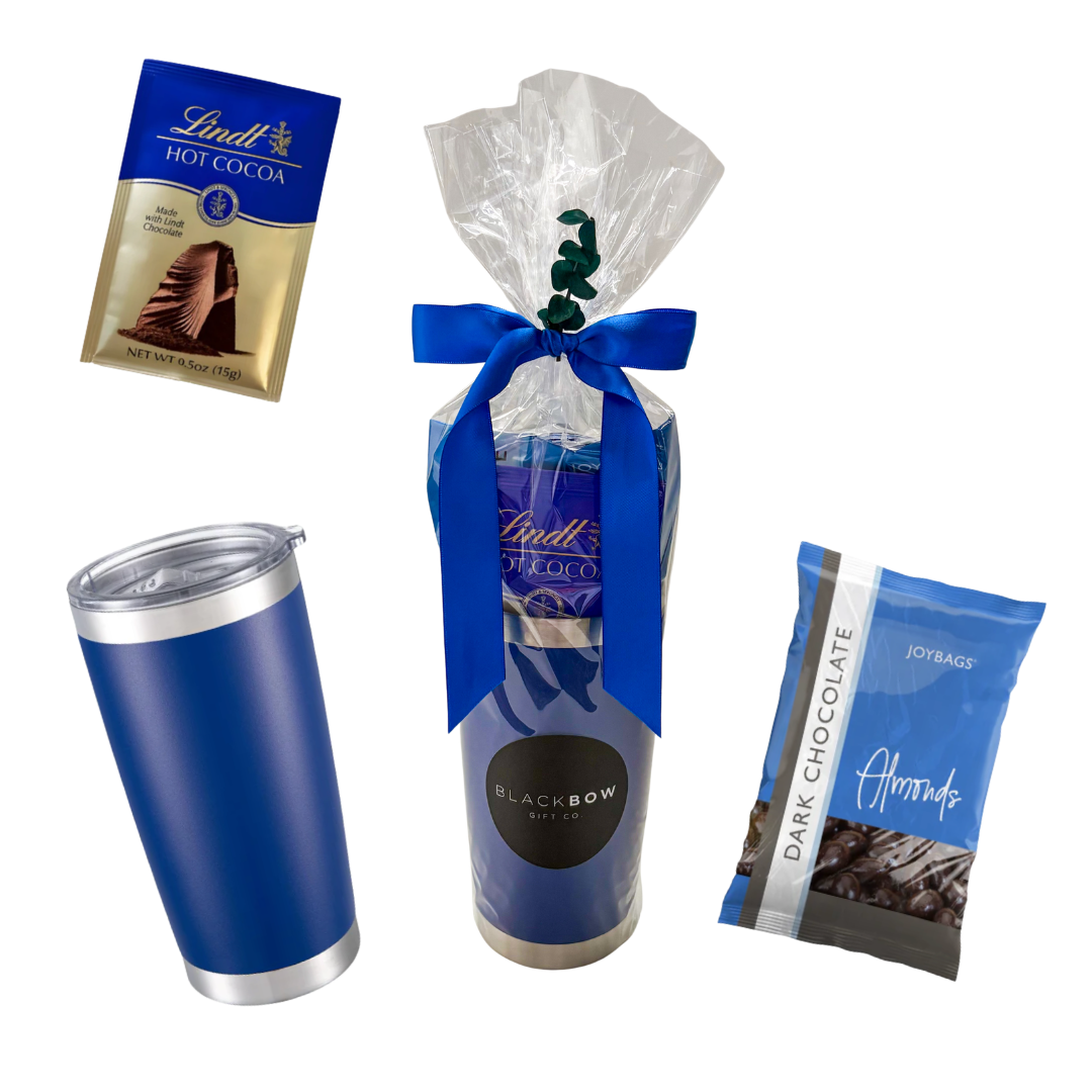 Blue tumbler gift featuring hot chocolate, sweet treats, and snack favourites presented in cello wrap with ribbon and decorative accents by Black Bow Gift Co.

