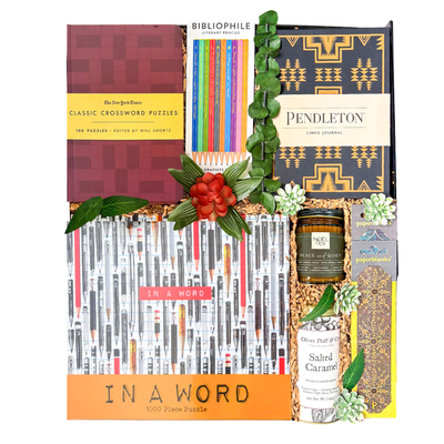 Luxury oversized high-gloss black magnetic gift box featuring optional books, crossword puzzle book, 1,000-piece puzzle, Pendleton journal, coloured pencils, insulated tumbler, gourmet coffee, artisan chocolates, candle, bookmark, and gifts for book lovers arranged in a layered presentation.