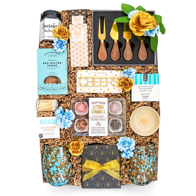 Luxury gourmet gift box featuring artisan treats, charcuterie accessories, serving pieces, decorative glassware, candle, and entertaining essentials by Black Bow Gift Co.