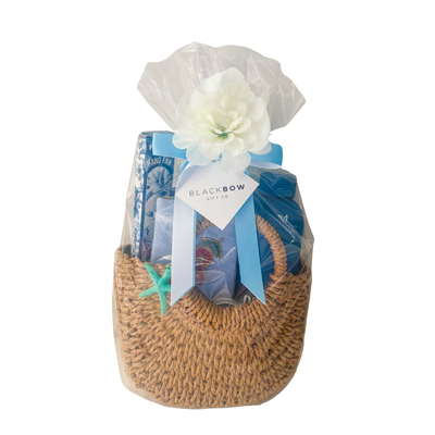 Beach-inspired gift purse featuring insulated water bottle, hand fan, eye mask, self-care essentials, and woven purse presentation by Black Bow Gift Co.