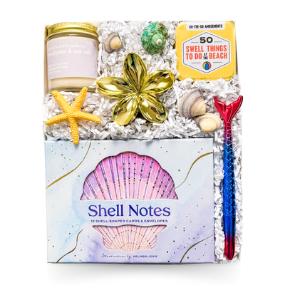 Luxury coastal gift box featuring shell stationery, coastal soy candle, beach activity cards, decorative seashells, floral trinket dish, mermaid pen, and seaside-inspired keepsakes.