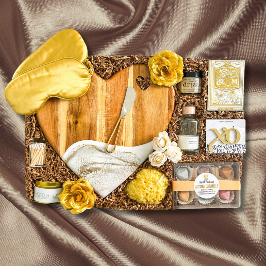 Gourmet gift basket with wooden board, gold eye mask, and various items on a satin background. Promotion highlighting wedding gift delivery across Canada for couples, clients, and celebrations.