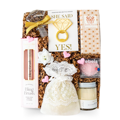 Bride to be gift box featuring a diamond ring bottle opener, jewelry cleaner, pearl scrunchie in a keepsake pouch, body butter, lip balm and artisan chocolate by Black Bow Gift Co.