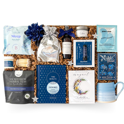 Gifting box with wellness products including tea, candles, and books on a white background