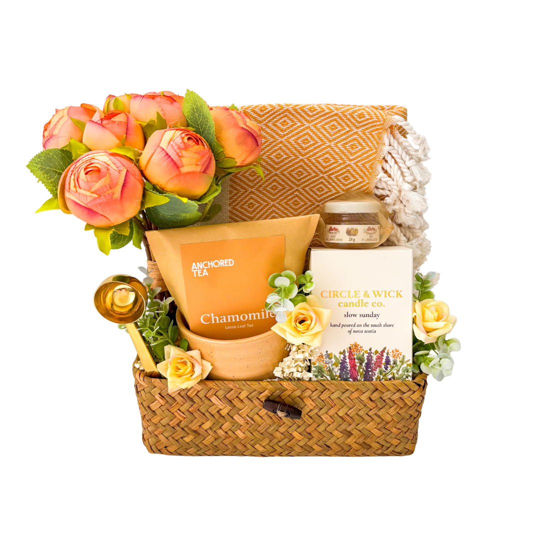 Seagrass relaxation gift basket featuring chamomile tea, local honey, hand-poured soy candle, cozy throw blanket, gold spoon, floral arrangement, and comforting self-care essentials.

