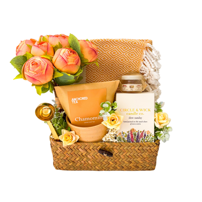Seagrass relaxation gift basket featuring chamomile tea, local honey, hand-poured soy candle, cozy throw blanket, gold spoon, floral arrangement, and comforting self-care essentials.