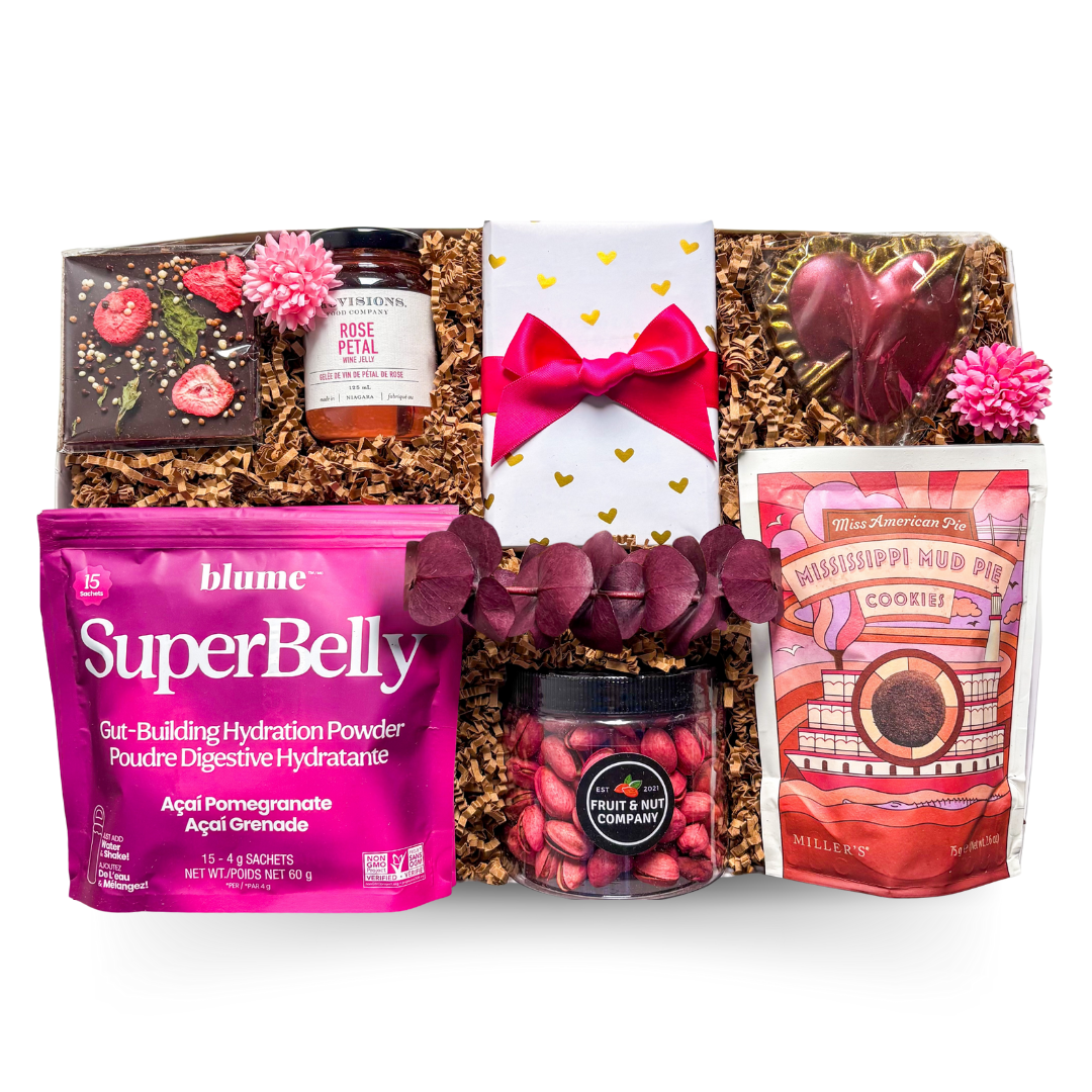An XL gift box tied with a satin ribbon and accented with dried florals, filled with pink, red, and purple gourmet treats including chocolate, rose jelly, pistachios, biscuits, and drink mix, creating a bright and joyful presentation with a polished, celebratory feel.
