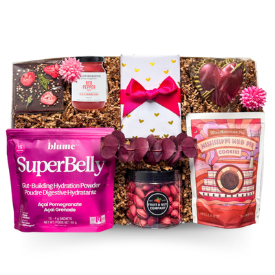 An XL gift box tied with a satin ribbon and accented with dried florals, filled with pink, red, and purple gourmet treats including chocolate, rose jelly, pistachios, biscuits, and drink mix, creating a bright and joyful presentation with a polished, celebratory feel.