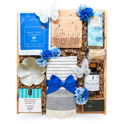 Luxury relaxation gift in a wooden keepsake box featuring artisan Earl Grey tea, handcrafted chocolate, pure Canadian maple syrup, soy candle, decorative wood coasters, cozy kitchen towel, ceramic trinket dish, and calming home essentials.